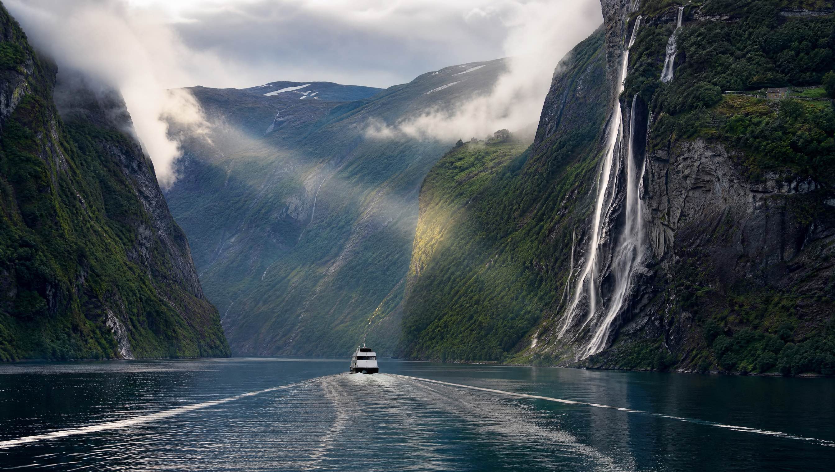 A ferry beneath the waterfalls of Geirangerfjord
