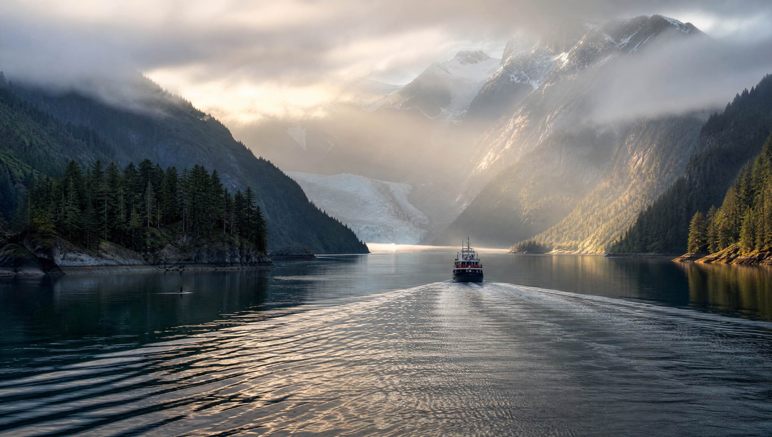 A vessel sailing through misty mountains and forest in Alaska’s Inside Passage